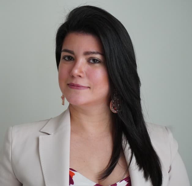 Woman with long dark hair wearing a beige blazer and patterned top, smiling for headshot.